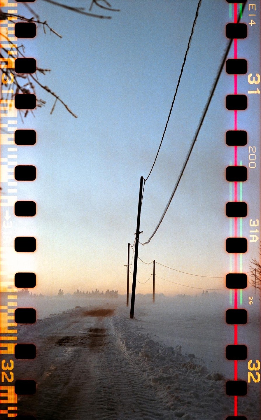 A snowy road with telephone poles leads into a foggy sunset.