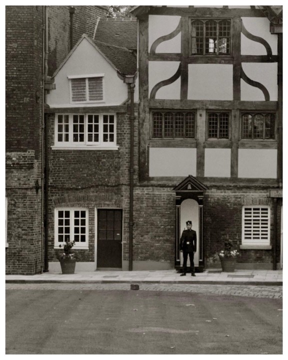 A guard stands at attention in a sentry box in front of a brick building with timber framing.