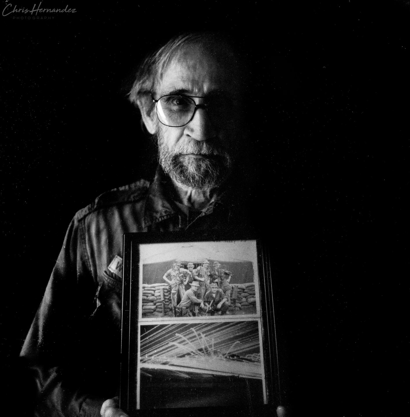A man with a beard and glasses holds a framed photograph of soldiers.