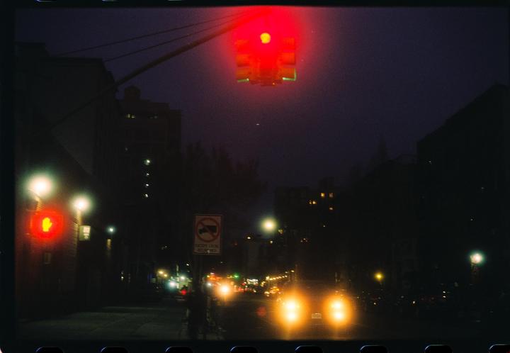 A red traffic light hangs over a street at night with car headlights visible in the distance.