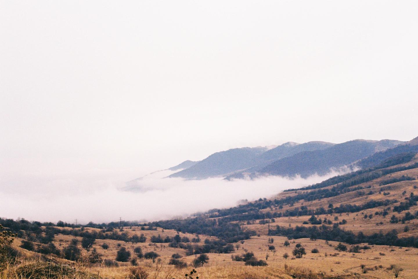 A landscape shows a valley filled with fog and mountains in the background.