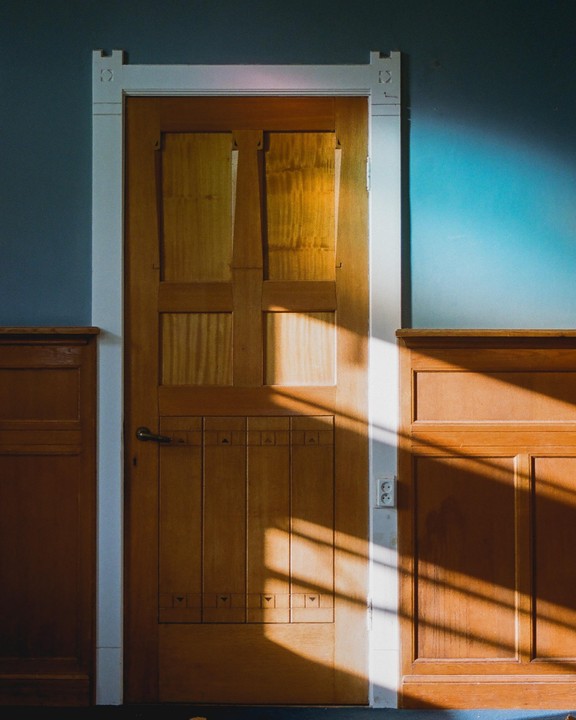 Sunlight streams through a window, casting shadows on a wooden door and wall.