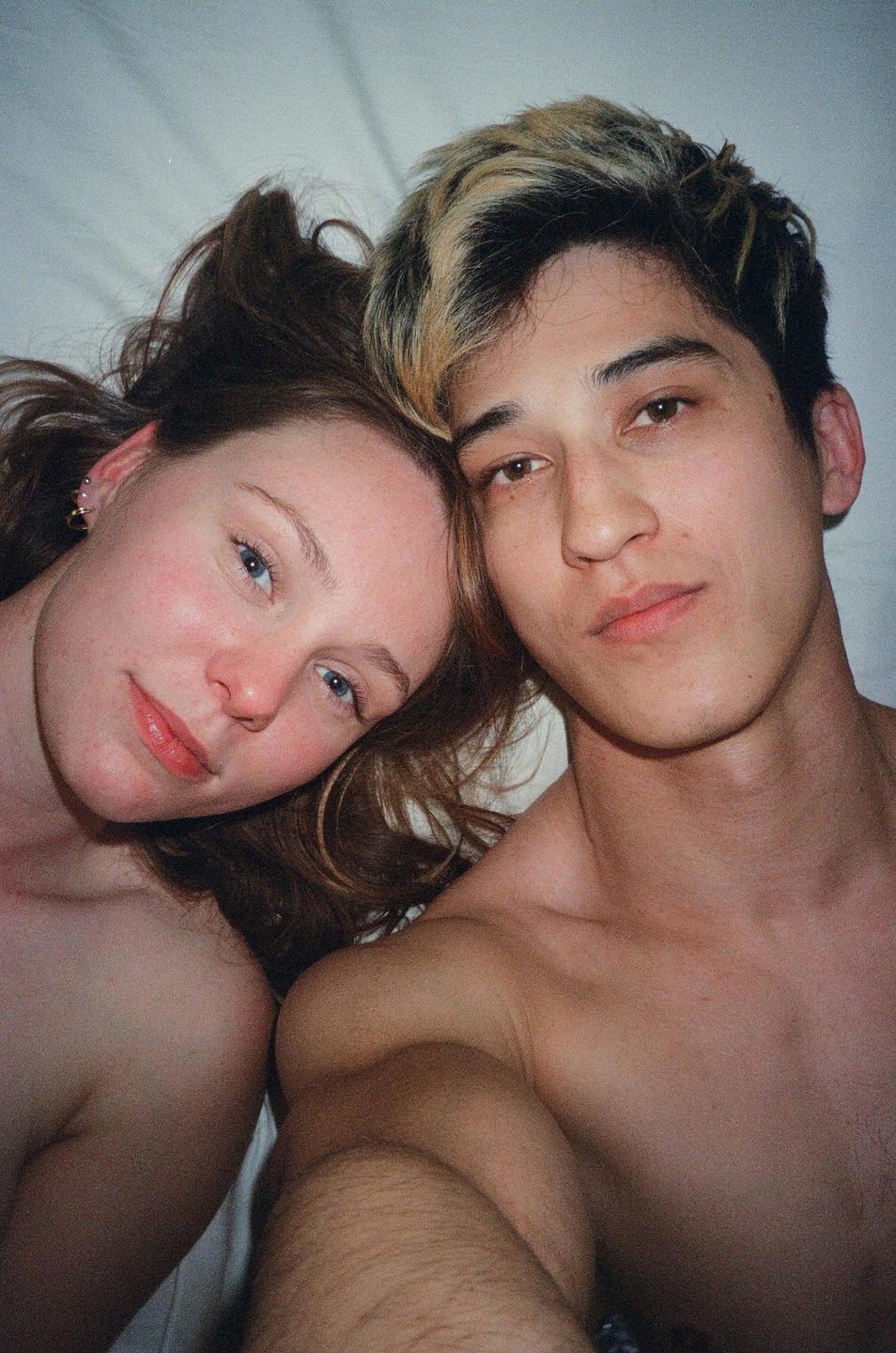 A couple lies close together, looking up at the camera.