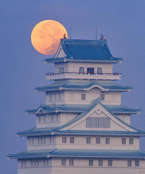 A large red moon is visible behind a multi-tiered Japanese castle with blue roofs.