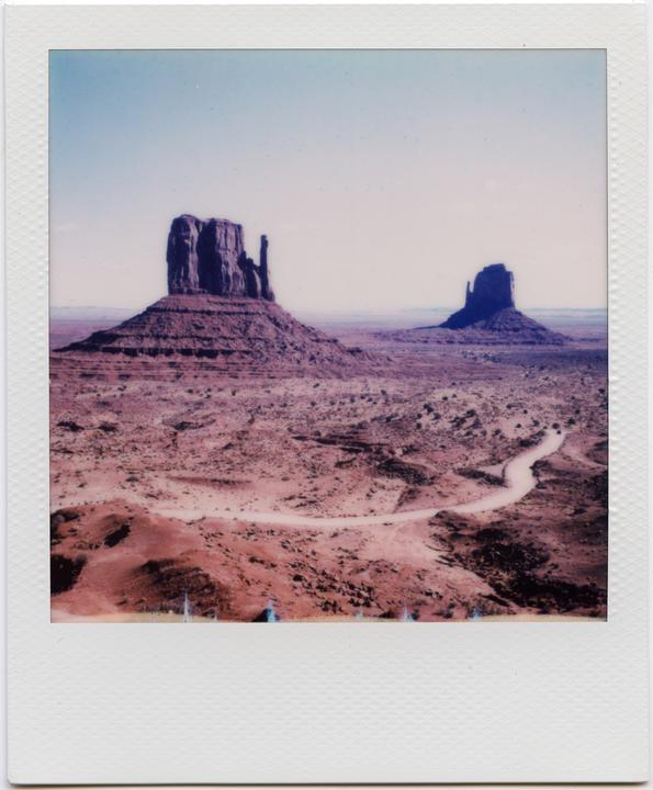 Two large rock formations stand in a vast desert landscape with a winding dirt road.