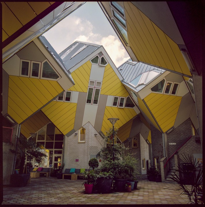 A courtyard is surrounded by yellow and gray cube houses with many windows.