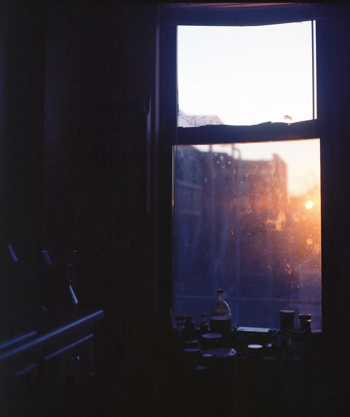 A window in a kitchen is illuminated by the setting sun, with bottles and containers on the sill.