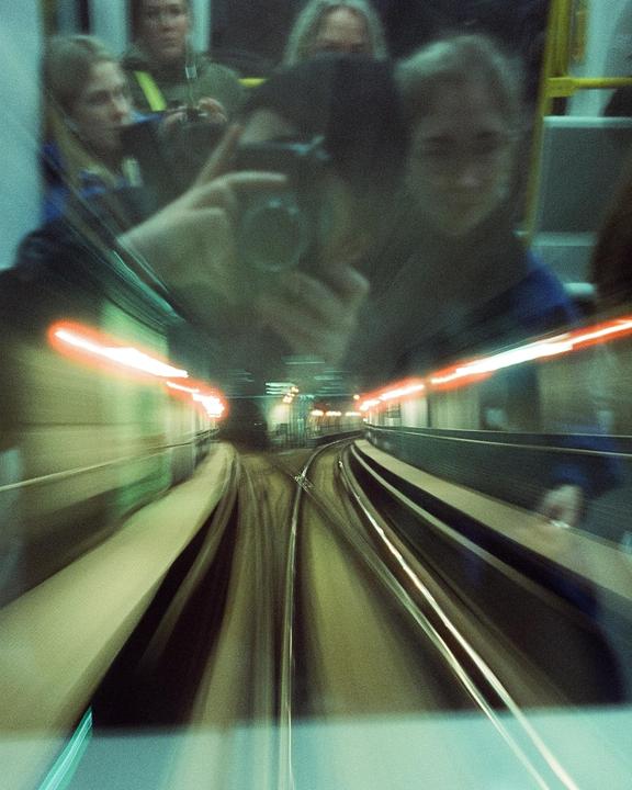 A person takes a self-portrait in a metro car, with the tracks visible through the front window.
