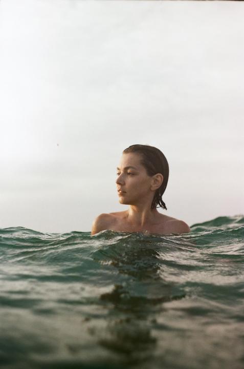 A woman with wet hair is in the ocean with waves around her shoulders.
