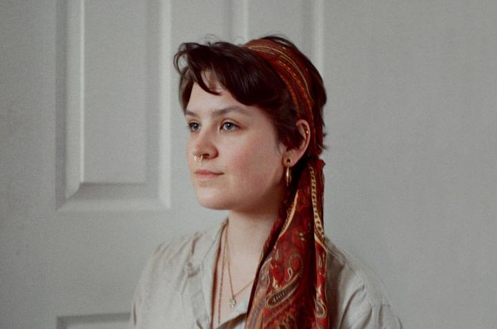 A woman with a red patterned headscarf and nose ring looks to the side in a self-portrait.