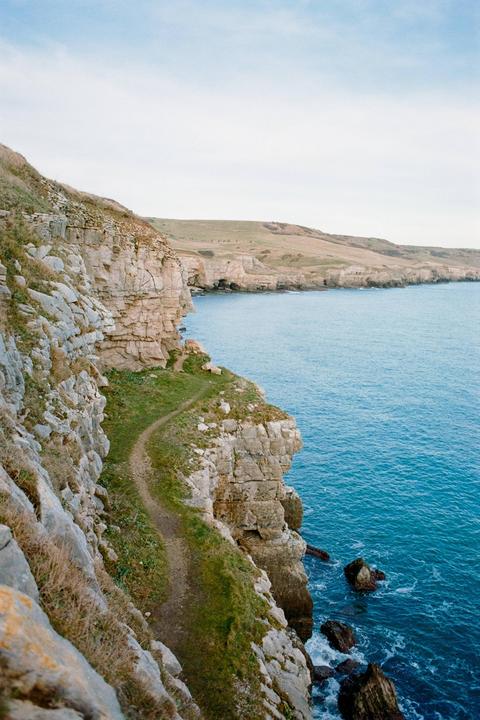 A narrow path winds along a rocky cliff overlooking a blue ocean.