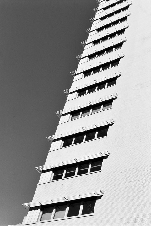 A tall building with many windows and awnings is angled against a clear sky.