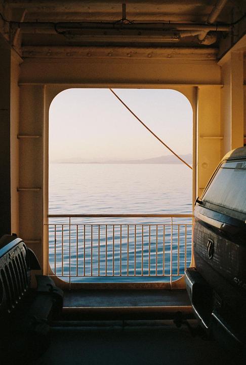 A view of the sea and distant mountains from inside a ferry with vehicles parked on deck.
