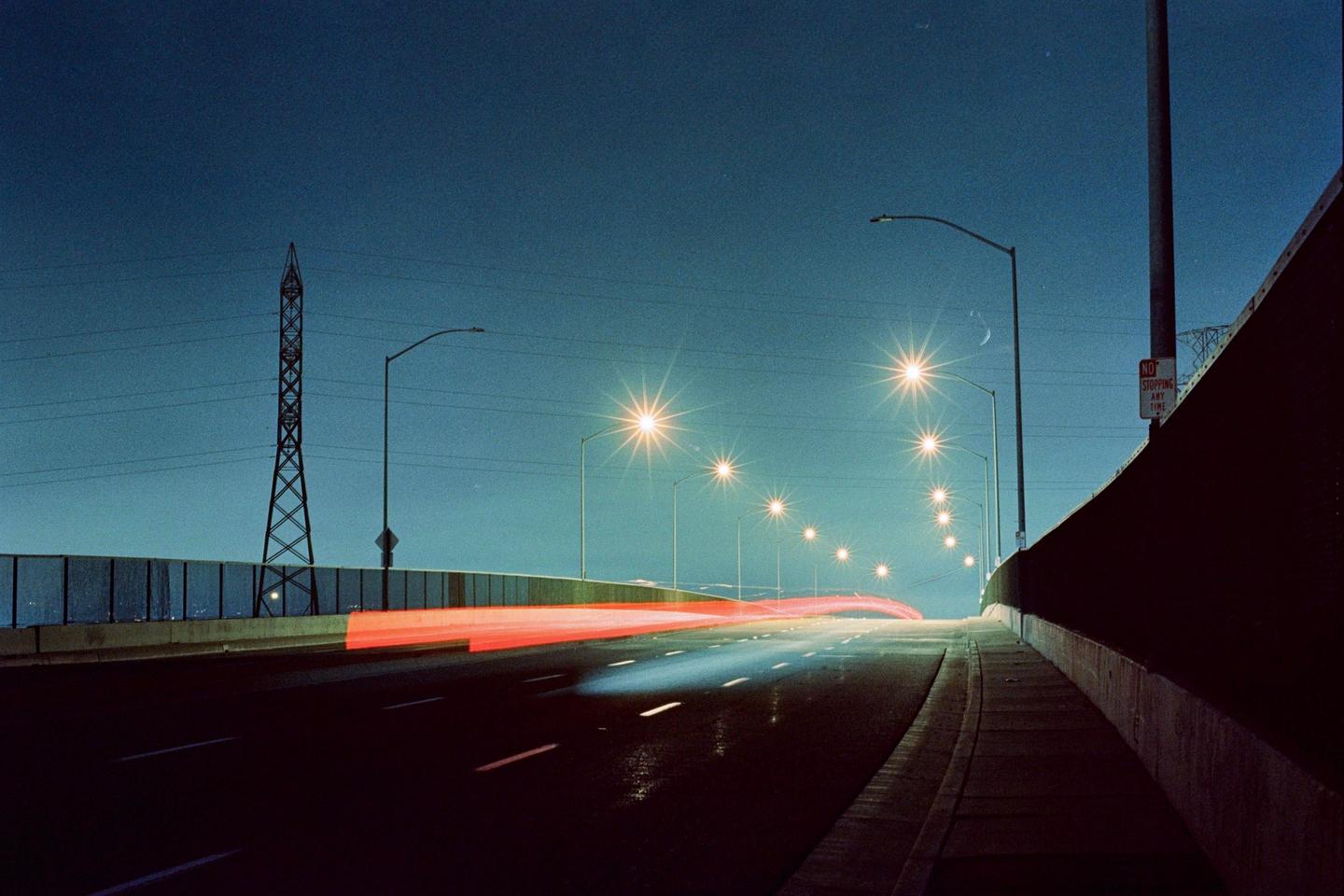A long exposure photograph captures light trails from vehicles on an overpass at night, with a crescent moon visible in the sky.