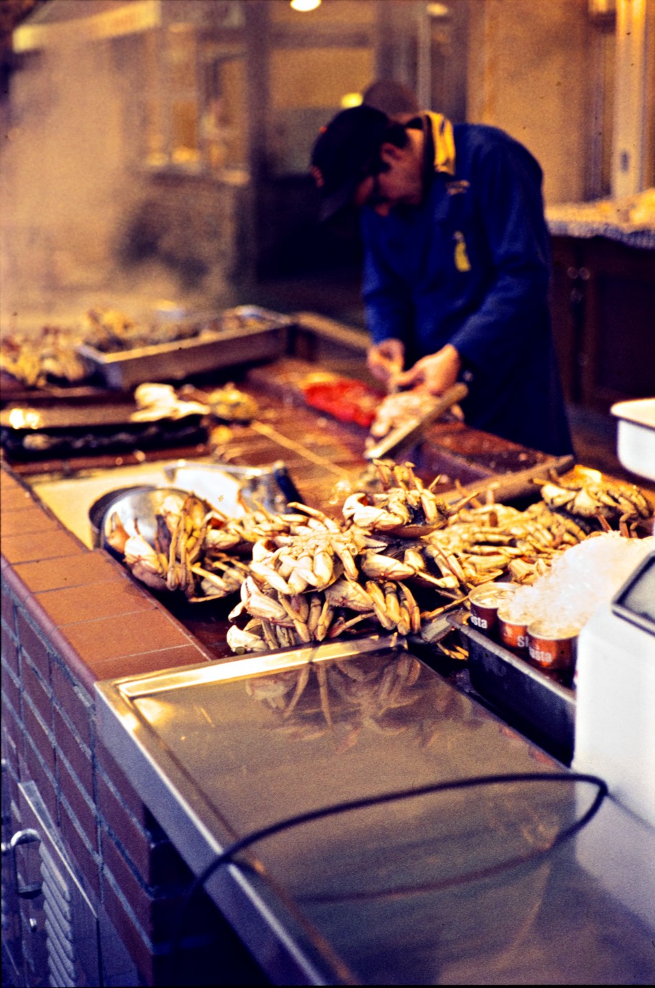 A man in a blue coat and a baseball cap prepares crabs on a street food stall.