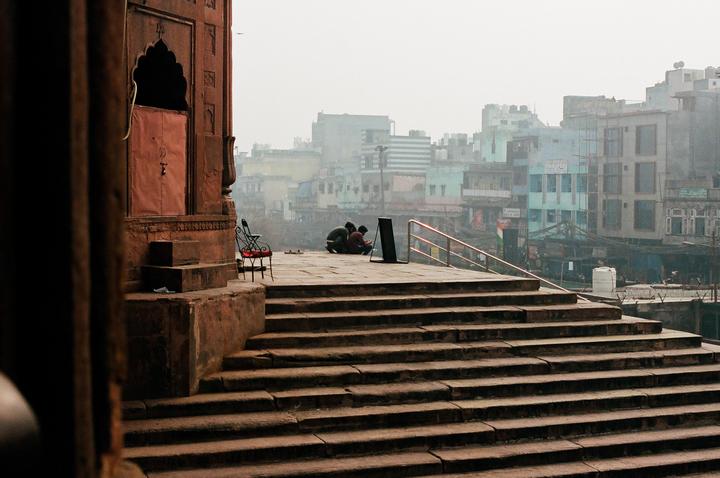 Three men are sitting on a stone platform with a city in the background, viewed from a stone staircase.