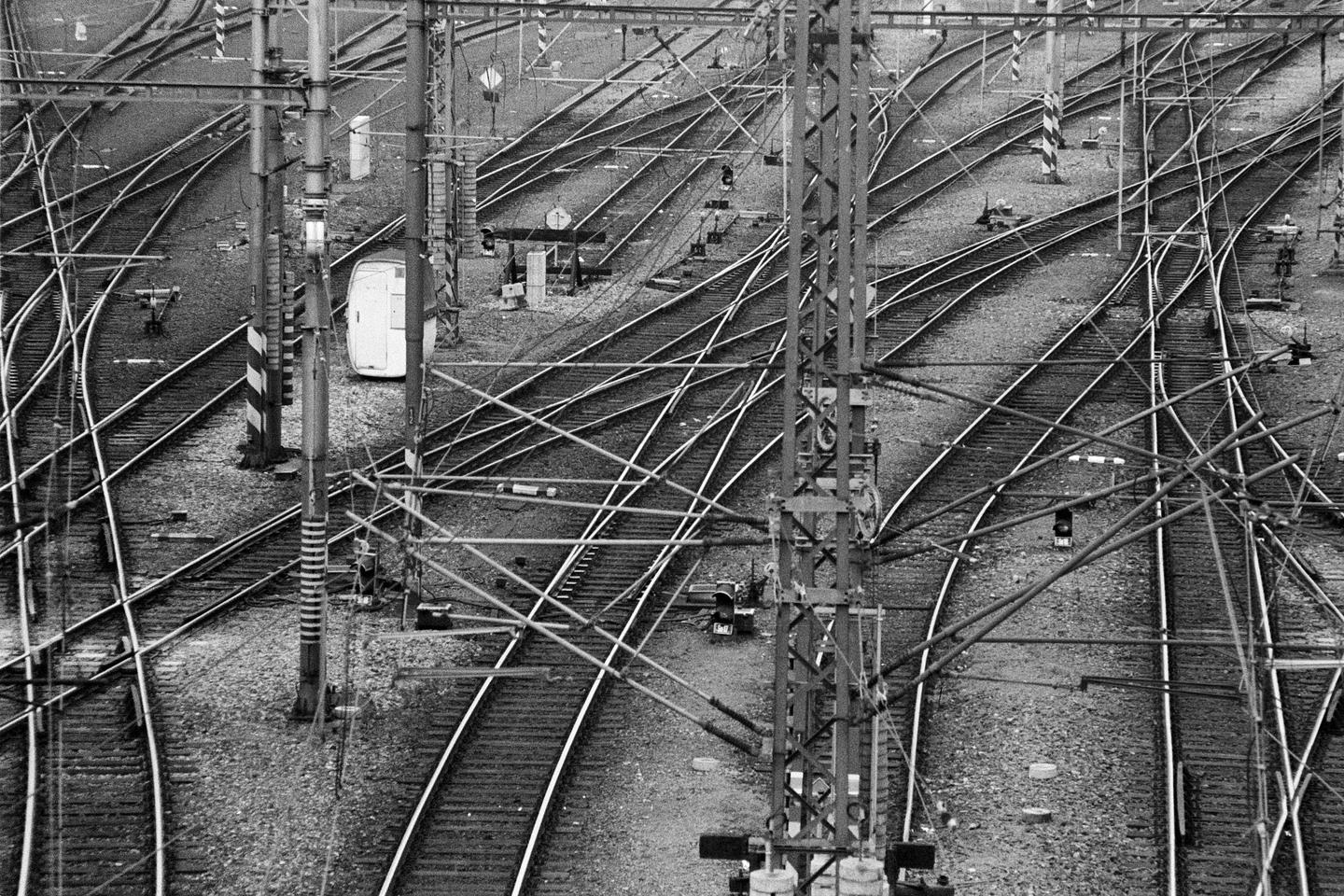 A complex network of railway tracks and overhead lines stretches across the frame, with a small white structure visible in the distance.