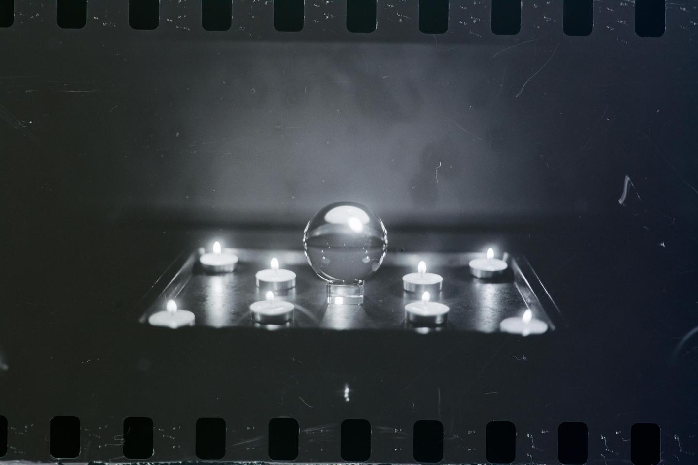 A crystal ball is surrounded by lit tea light candles on a reflective surface.