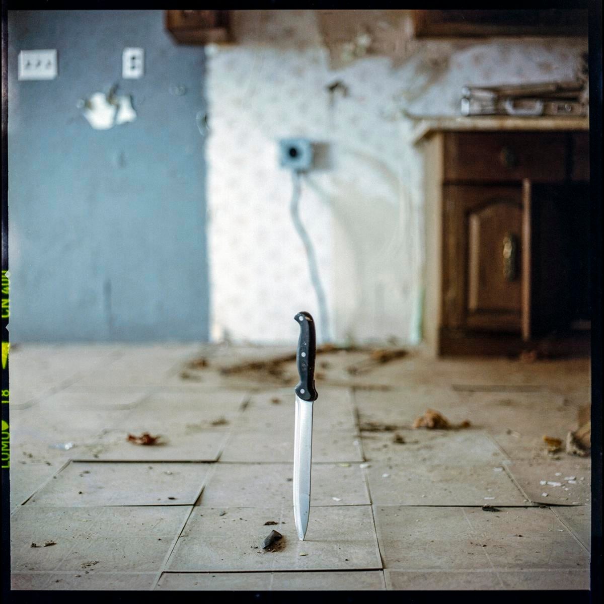 A knife is stuck upright in the tiled floor of a dilapidated room.