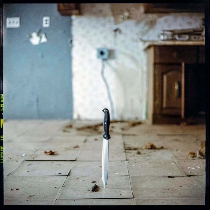A knife is stuck upright in the tiled floor of a dilapidated room.