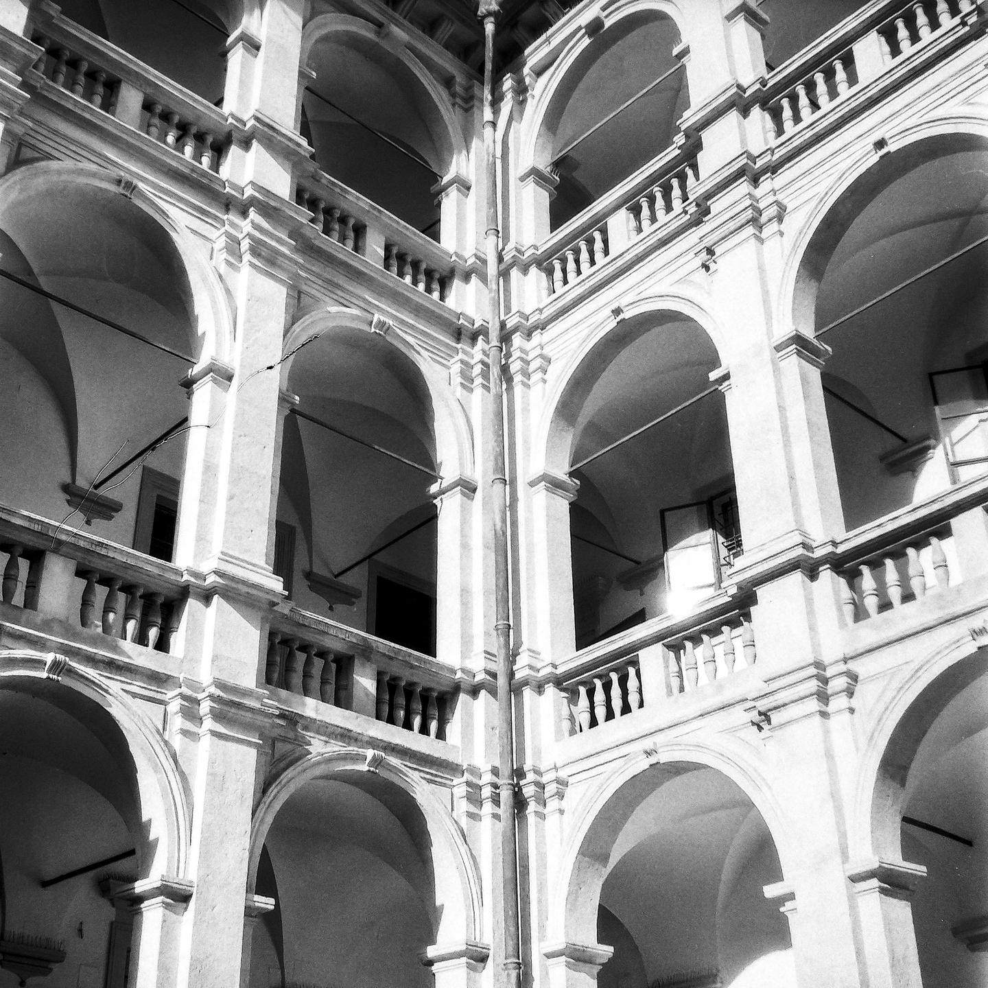 A multi-story building with arched walkways and balustrades is shown from an interior courtyard.
