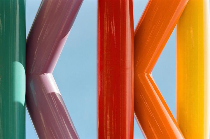 A colorful abstract image shows a series of vertical and diagonal metal beams against a clear blue sky.
