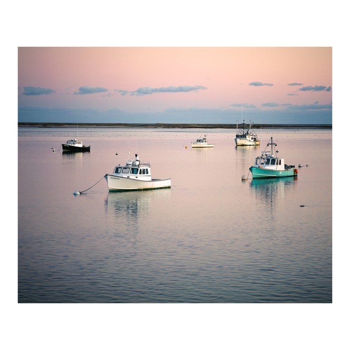 Several fishing boats are anchored in calm water under a pastel sky at dusk.