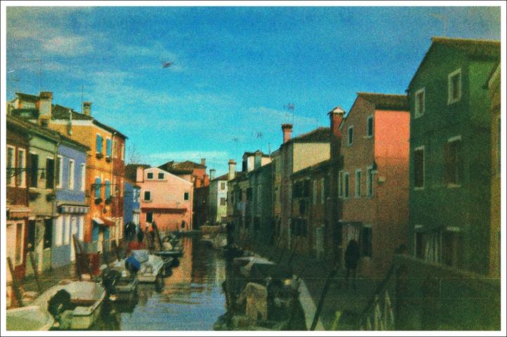 A canal with boats is lined by colorful buildings under a bright blue sky.