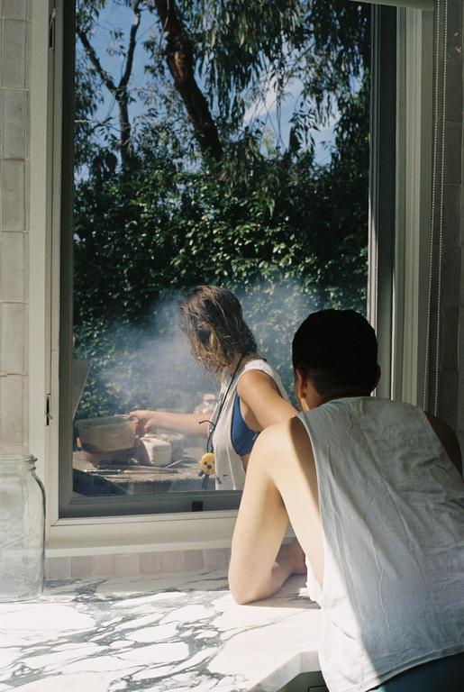 A woman and a man are looking out a window at a smoking grill.