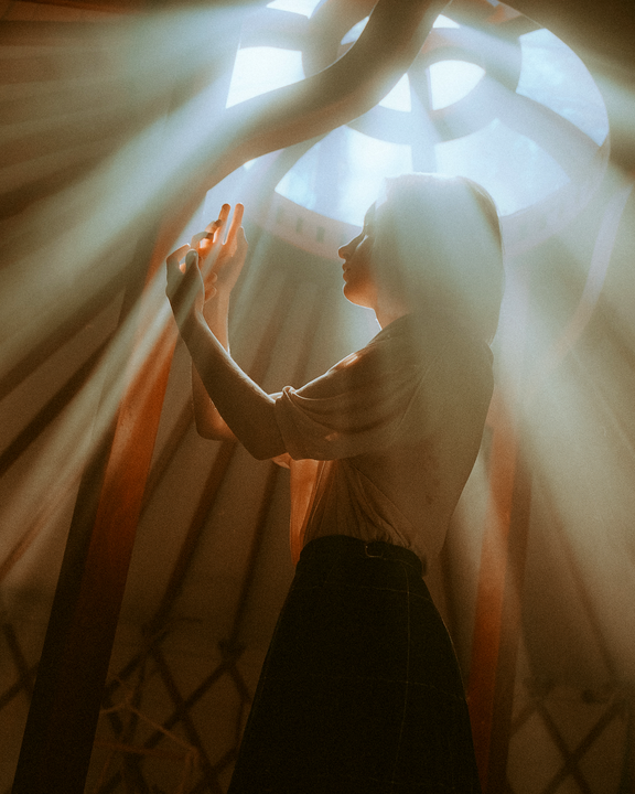A woman stands in a room with light rays shining through a circular window.