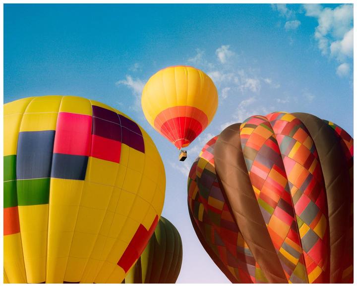 Several colorful hot air balloons are visible against a bright blue sky with scattered clouds.