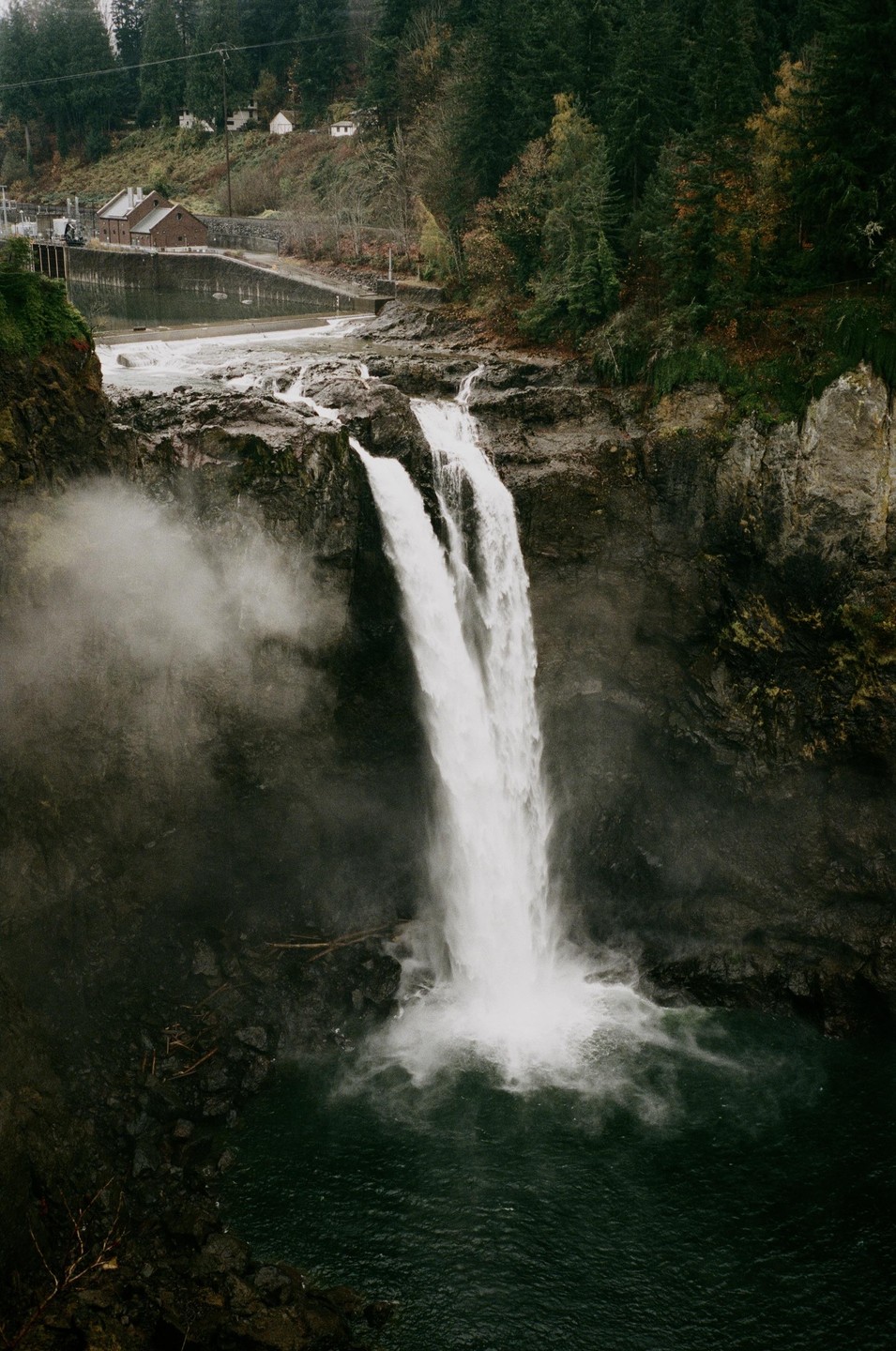 A powerful waterfall cascades into a dark pool, surrounded by rocky cliffs and a lush forest.