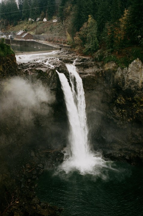 A powerful waterfall cascades into a dark pool, surrounded by rocky cliffs and a lush forest.