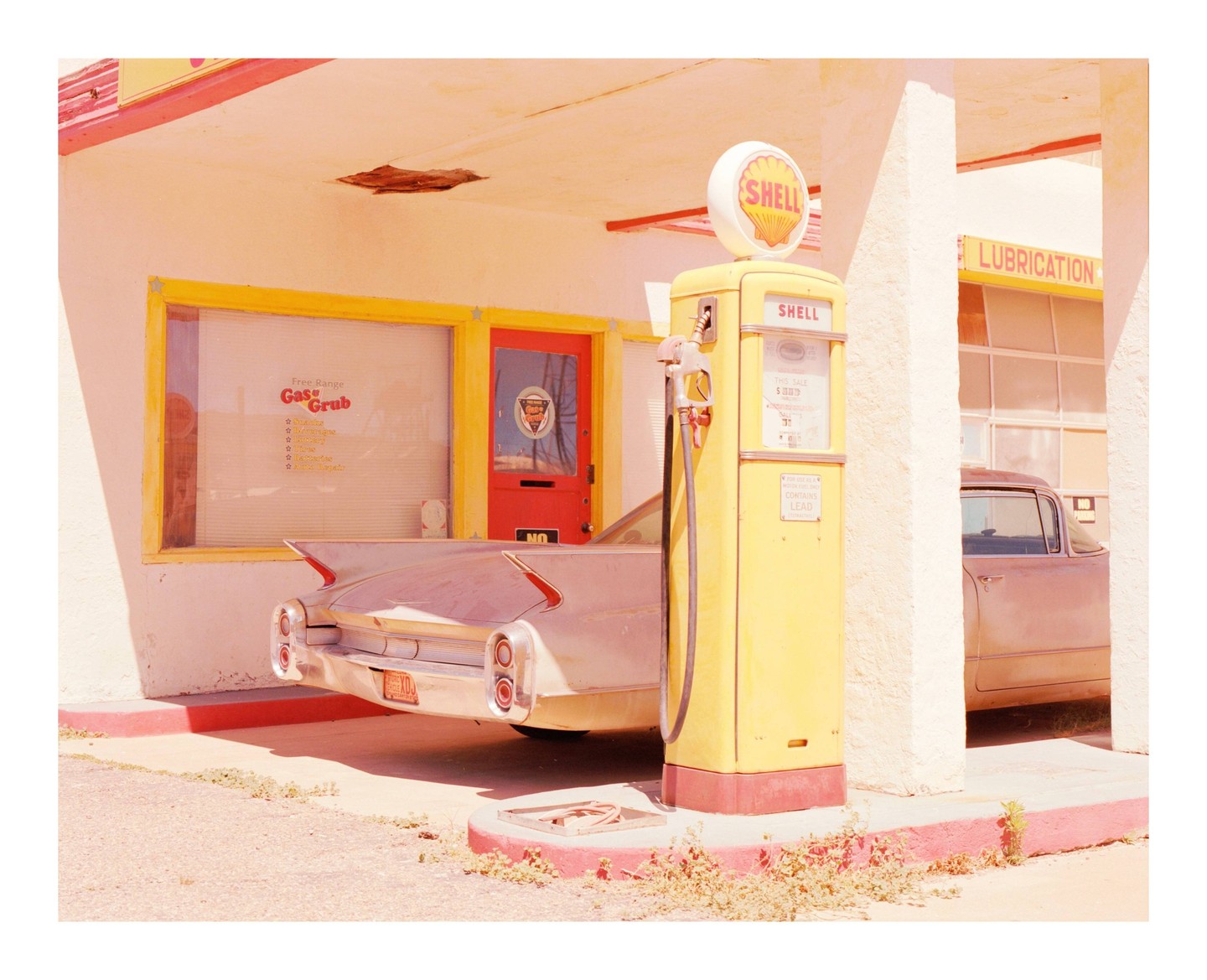 A vintage gas station with a yellow Shell gas pump and a classic car parked under the awning.