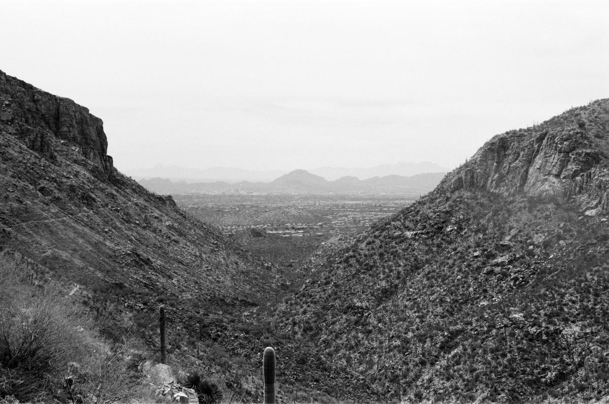 A valley with a city in the distance is visible between two mountains covered in desert vegetation.