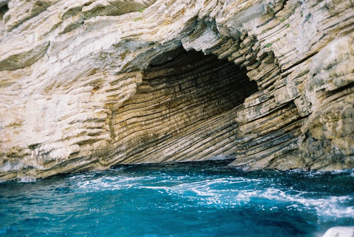 A cave entrance with layered rock formations is visible above turquoise water.