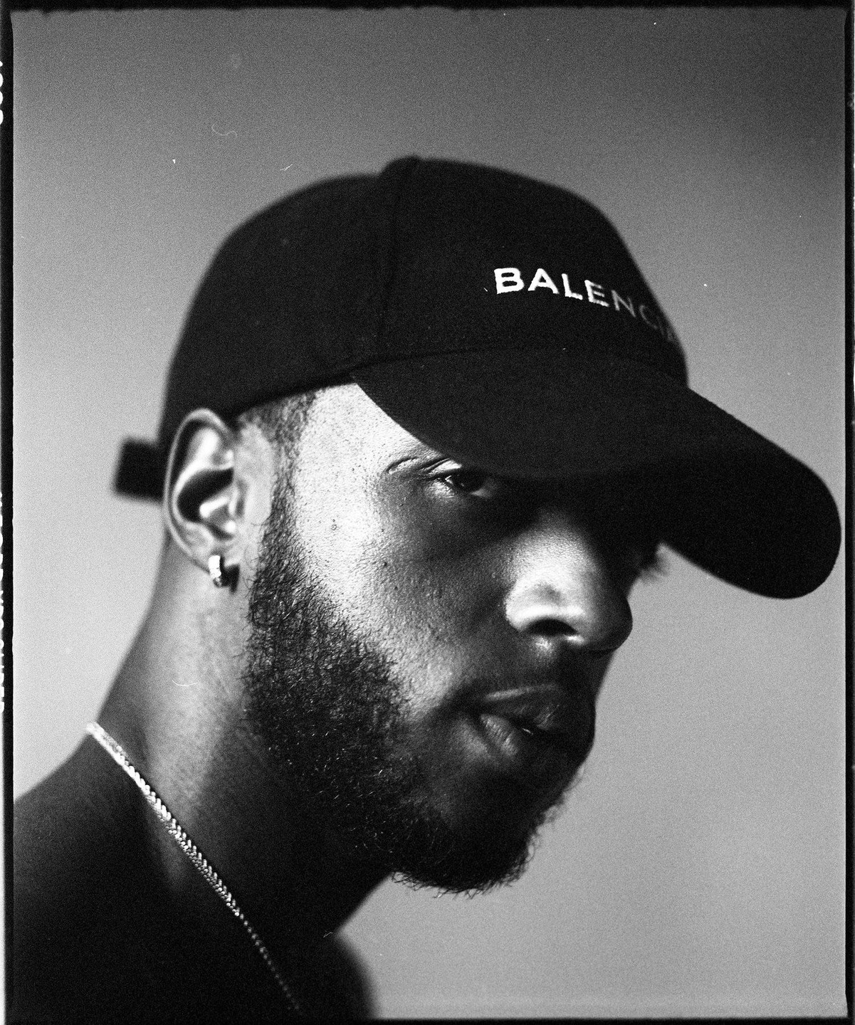 A man with a beard and a baseball cap looks to the right, with his face partially obscured by shadow.