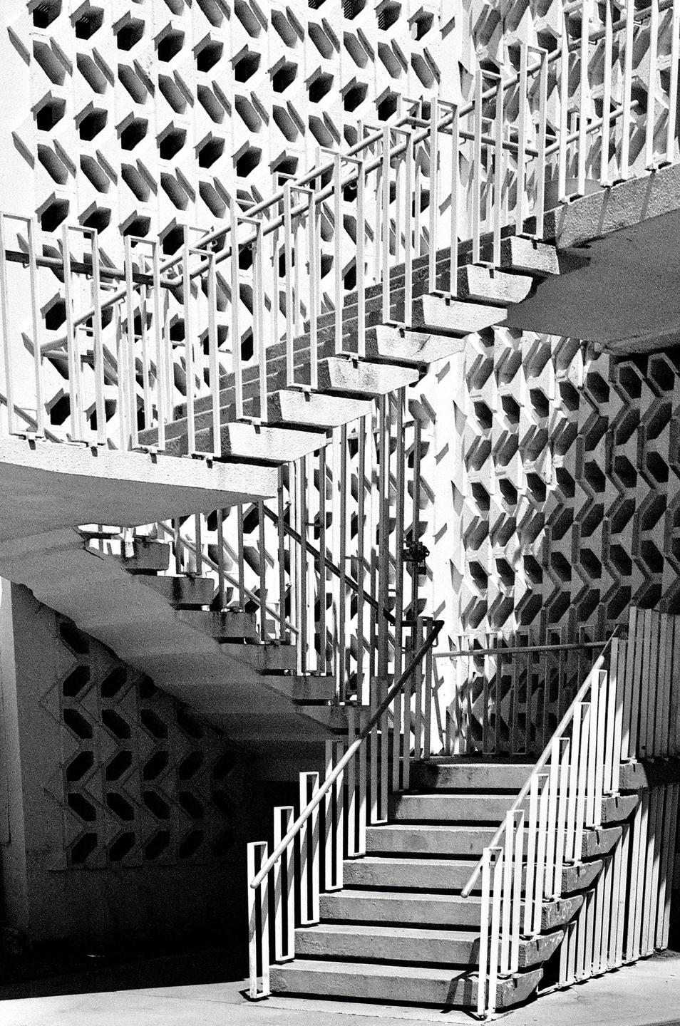 A multi-level outdoor staircase with white railings is set against a patterned wall.