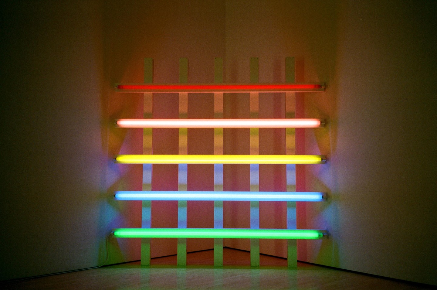 Five horizontal neon tubes in different colors are mounted on a grid against a wall.