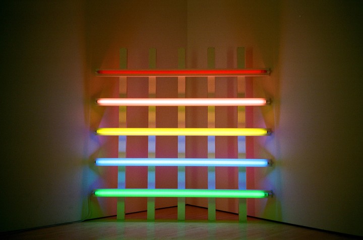 Five horizontal neon tubes in different colors are mounted on a grid against a wall.