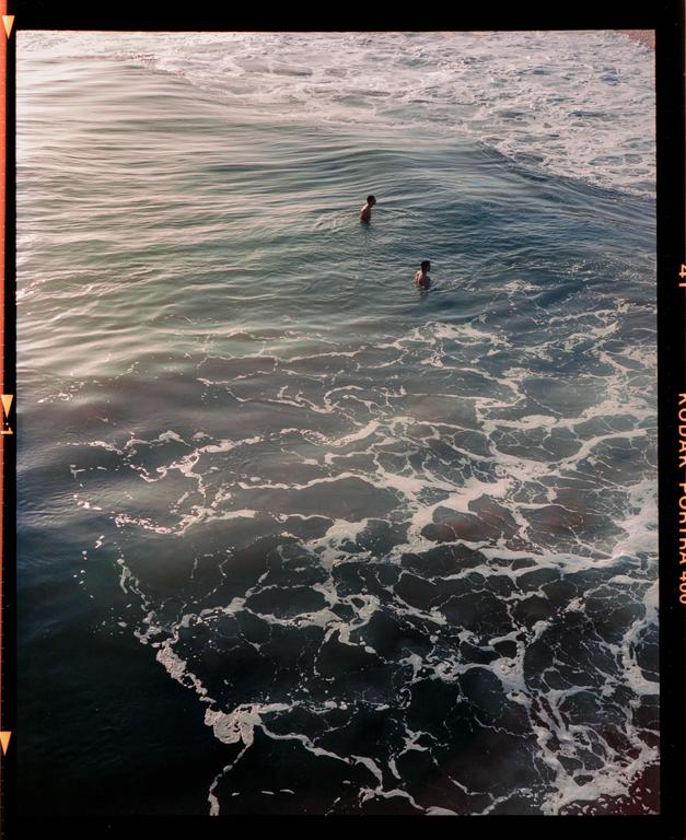 Two people are swimming in the ocean with foamy waves.