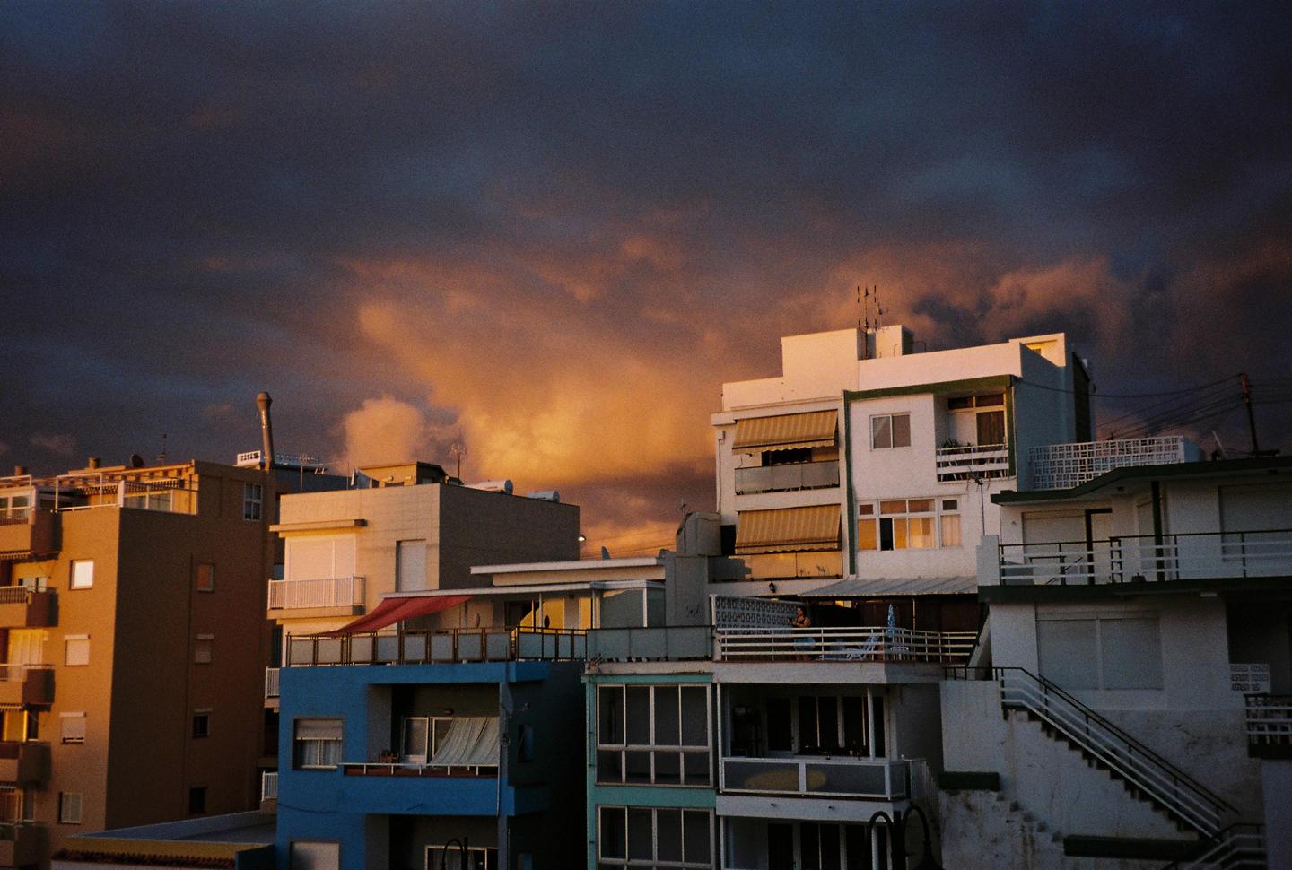 The last rays of sun illuminate the clouds above a cluster of buildings.