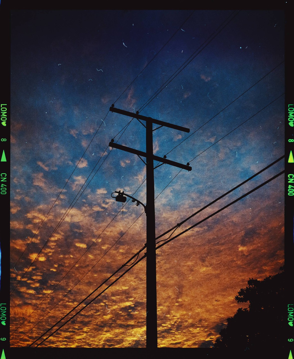 A utility pole and power lines are silhouetted against a dramatic sunset sky with orange and blue clouds.