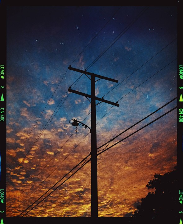 A utility pole and power lines are silhouetted against a dramatic sunset sky with orange and blue clouds.