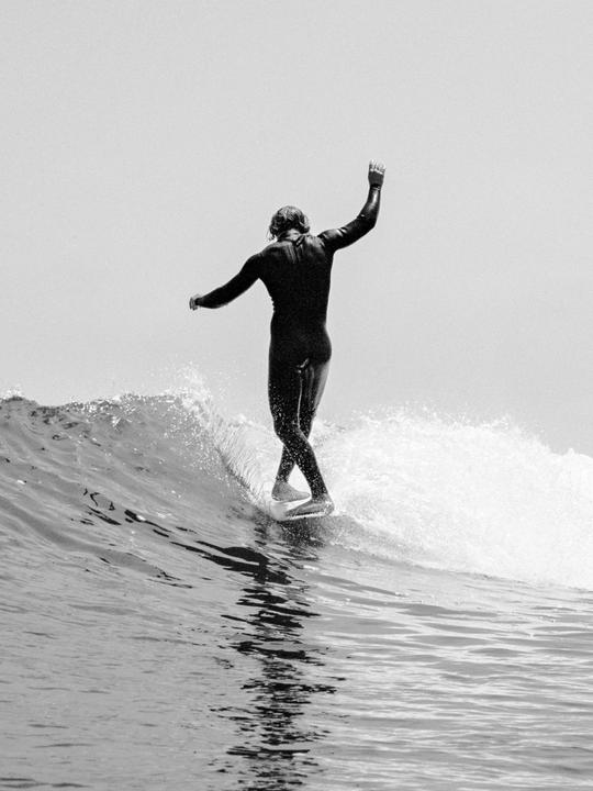 A surfer in a wetsuit rides a wave with arms outstretched.