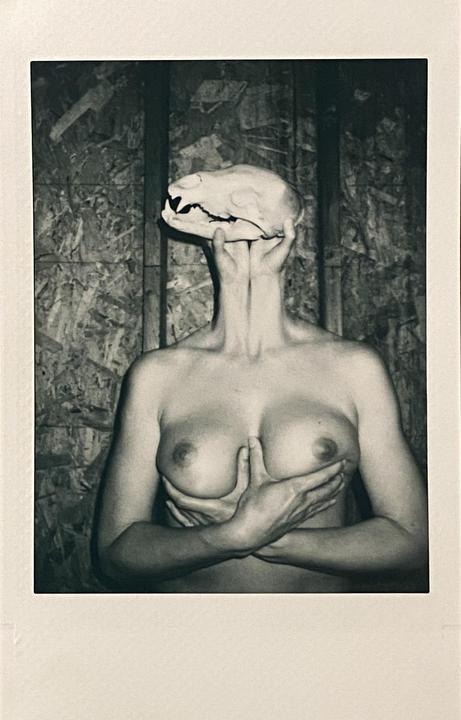 A person holds a skull over their head while covering their chest with their hands.