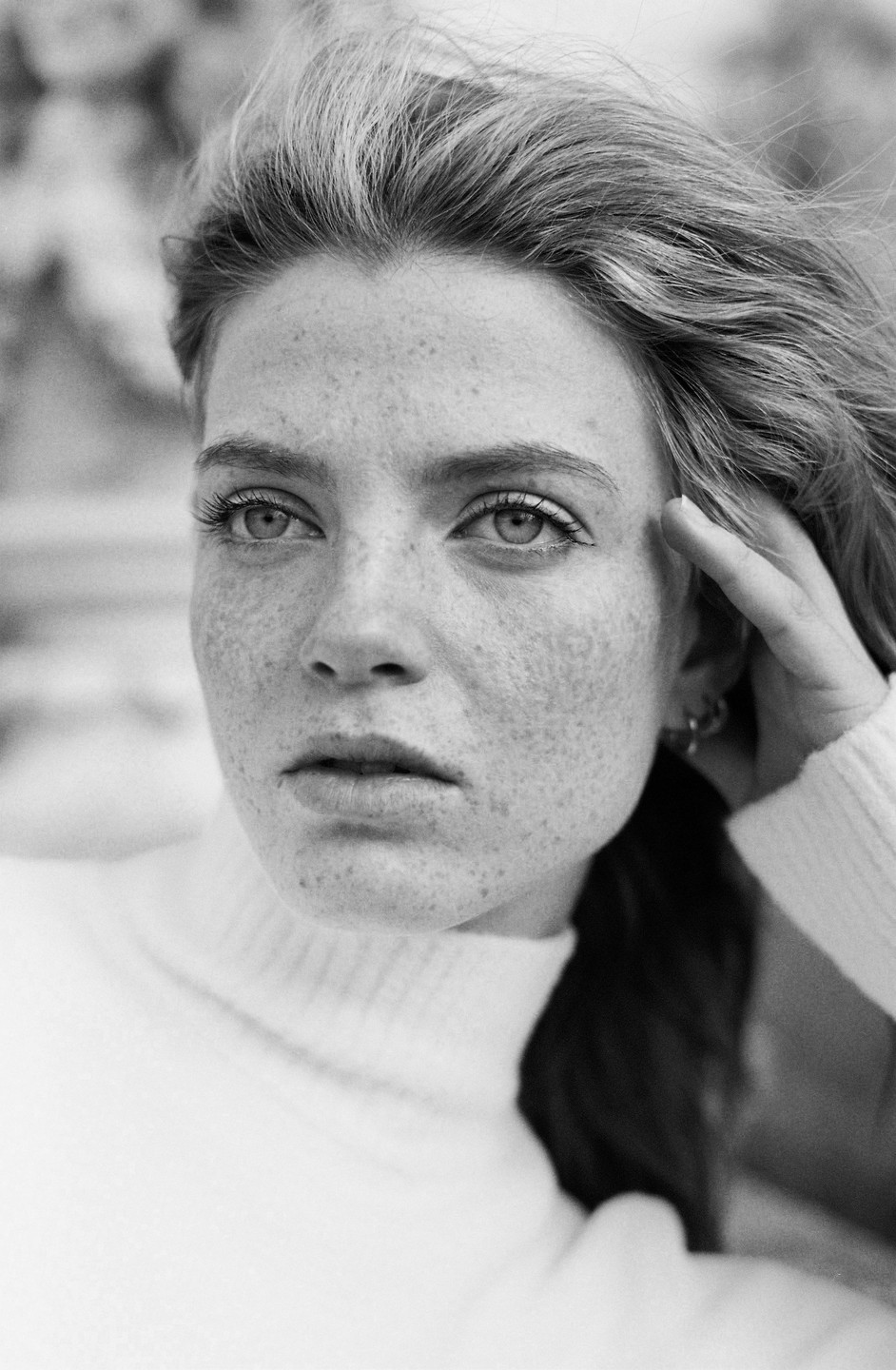 A woman with freckles and windblown hair looks directly at the viewer.
