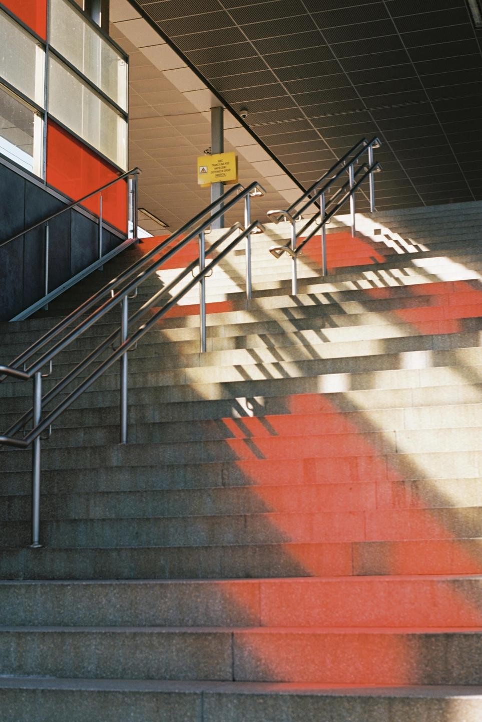 Sunlight casts shadows and red light onto a concrete staircase with metal railings.
