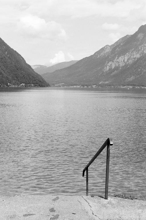 A metal handrail extends into a lake surrounded by mountains under a cloudy sky.