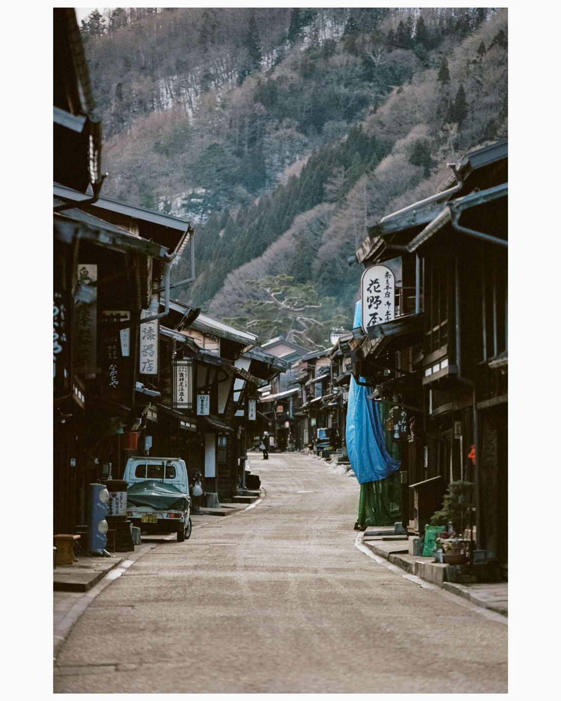 A narrow street lined with traditional Japanese buildings leads towards a snow-dusted mountain.